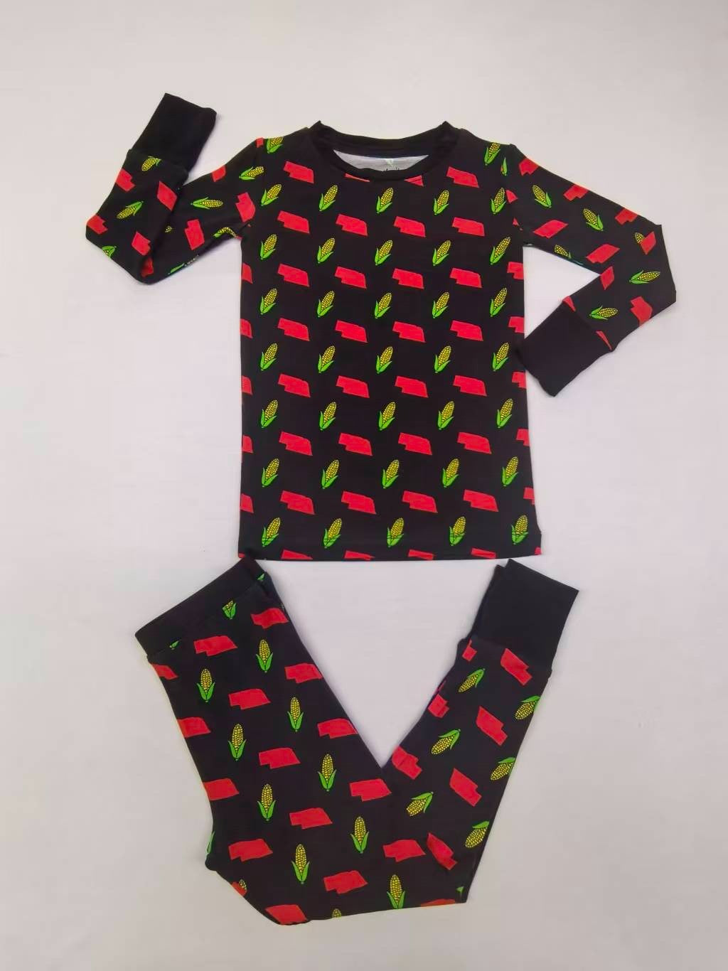 Children's pajama set with long sleeves, black base featuring red car and green leaf patterns.